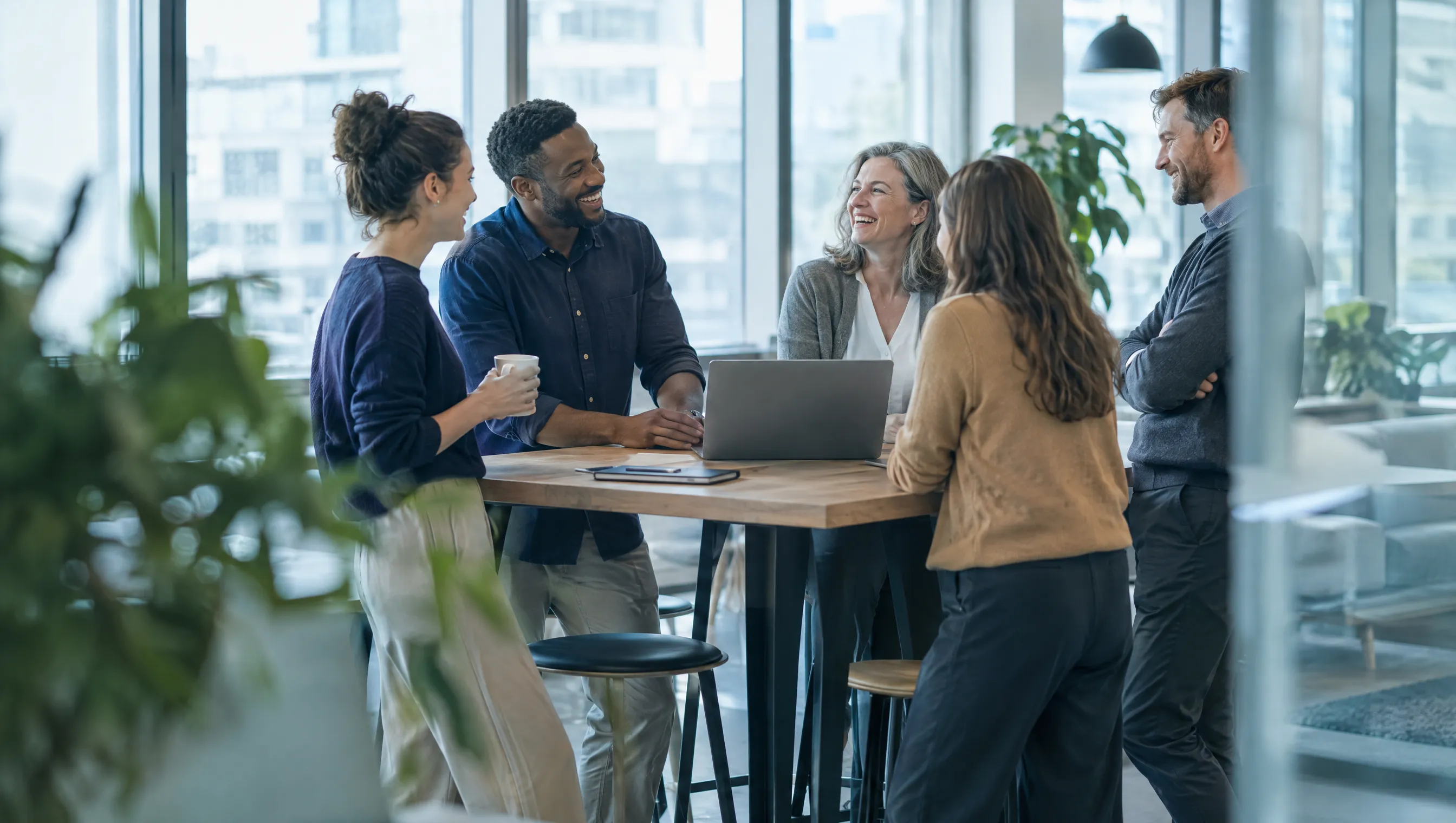 A small team laughing together around a table in a bright office